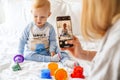 Mother taking photo of her blonde baby son on mobile phone Royalty Free Stock Photo