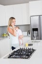 Mother talking on mobile phone while carrying her baby in kitchen Royalty Free Stock Photo