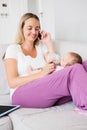 Mother talking on mobile phone while feeding her baby with milk bottle Royalty Free Stock Photo