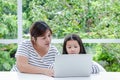 Mother taught a young Asian daughter to study online at home using a notebook computer.