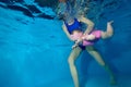 A mother teaches a baby girl to swim underwater. Charming little girl under the water in a red swimsuit on a blue