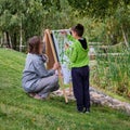 Mother teaches boy son to paint on canvas. Woman teacher artist paints with a child on paper nature and trees by the river Royalty Free Stock Photo