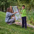 Mother teaches boy son to paint on canvas. Woman teacher artist paints with a child on paper nature and trees by the river Royalty Free Stock Photo