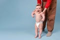 Mother teaches the child to stand on his feet and walk, baby boy on a studio blue background Royalty Free Stock Photo