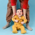 Mother teaches toddler baby to stand on his feet and sits, child boy on studio blue background Royalty Free Stock Photo