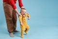 Mother teaches toddler baby to stand on his feet and walk, child boy on studio blue background Royalty Free Stock Photo