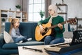 Mother teaching cute little musician girl to play guitar.