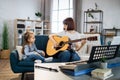 Mother teaching cute little musician girl to play guitar.