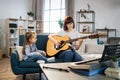 Mother teaching cute little musician girl to play guitar.