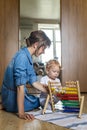 Mother teaching little kid counting on multi colored childish wooden ecological abacus on floor