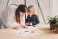 Mother teaching toddler boy to draw with pencils at home