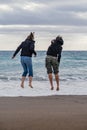 Mother and teenage daughter on the beach jumping on the waves. Rear view, vertical composition Royalty Free Stock Photo