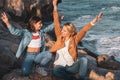 Mother and daughter sitting on the rocks by the mediterranean sea with arms raised playing with the air