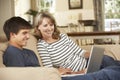 Mother With Teenage Son Sitting On Sofa At Home Using Laptop