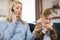 Mother with thermometer and cell phone while checking temperature of her sick teen son Royalty Free Stock Photo