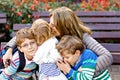 Mother and three children hugging. Happy family sitting outdoor: woman and two brother kids boys and cute little toddler