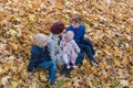 Mother and three children sitting on fallen leaves in autumn forest. Family walking in fall Park Royalty Free Stock Photo