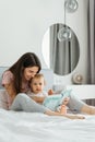 Mother and toddler daughter reading fairytale book in bedroom