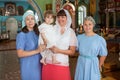 Mother with toddler and teenage daughters standing in the Orthodox church, godmother holding her goddaughter in arms