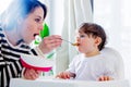 Mother try to feeding a toddler boy with a spoon in a chair Royalty Free Stock Photo