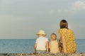 Mother with two children sitting on the beach and looking out to sea. Back view. Summer vacation with children Royalty Free Stock Photo