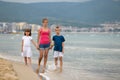 Mother and two children son and daughter walking together on sand beach in sea water in summer with bare feet in warm ocean waves Royalty Free Stock Photo