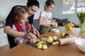 A mother and two daughters cook apple pie filling together at the table, a mother teaches her daughter to cook.