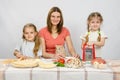 Mother and two little girls at table prepared ingredients for the pizza. They were watching a cat