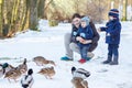 Mother and two little siblings boys feeding ducks in winter. Royalty Free Stock Photo