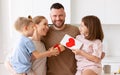 Mother and two smiling kids congratulating dad with Fathers day while standing in kitchen in morning Royalty Free Stock Photo