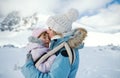 Mother with unhappy small daughter in carrier standing in winter nature, kissing.