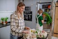 Mother unpacking local food in zero waste packaging from bag with help of daughter in kitchen at home.