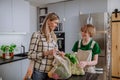 Mother unpacking local food in zero waste packaging from bag with help of daughter in kitchen at home.