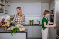 Mother unpacking local food in zero waste packaging from bag with help of daughter in kitchen at home.