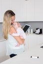 Mother using digital tablet while carrying her baby in kitchen Royalty Free Stock Photo