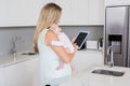 Mother using digital tablet while carrying her baby in kitchen