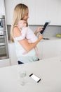 Mother using digital tablet while carrying her baby in kitchen Royalty Free Stock Photo