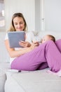 Mother using digital tablet while feeding her baby with milk bottle Royalty Free Stock Photo