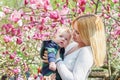 Mother walking with her baby son in garden of blooming magnolias