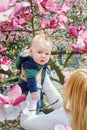 Mother walking with her baby son in garden of blooming magnolias