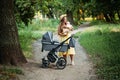 Mother walking with Newborn baby in Bassinet stroller in summer park in sunny day. Strollers for Newborns. Keep baby Royalty Free Stock Photo