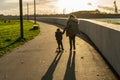 A mother walking on the pavement with her young son riding a scooter next to her holding his hand at sunset Royalty Free Stock Photo
