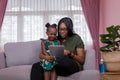 Mother was teaching the daughter through tablet joyfully while sitting on the sofa. black people or African Americans. Home study Royalty Free Stock Photo