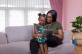 Mother was teaching the daughter through tablet joyfully while sitting on the sofa. black people or African Americans. Home study Royalty Free Stock Photo