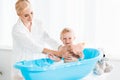Mother washing cheerful toddler son holding bottle with shampoo