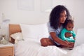 Mother Wearing Pyjamas With Baby Daughter In Bedroom Working From Home On Laptop