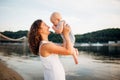 Mother which turns the child against a sunset and water. Happy mom and baby. Playing on beach. Young woman tossing up her son Royalty Free Stock Photo