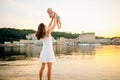 Mother which turns the child against a sunset and water. Happy mom and baby. Playing on beach. Young woman tossing up her son Royalty Free Stock Photo