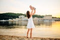 Mother which turns the child against a sunset and water. Happy mom and baby. Playing on beach. Young woman tossing up her son Royalty Free Stock Photo