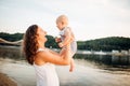 Mother which turns the child against a sunset and water. Happy mom and baby. Playing on beach. Young woman tossing up her son Royalty Free Stock Photo